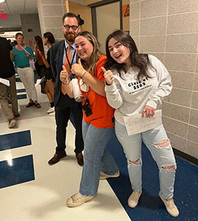 Two female high school students with their thumbs up standing hall with Dr. Greenwood